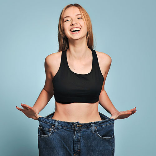 A woman shows her weight loss success after following a Zen Care Physical Medicine-guided wellness program.
